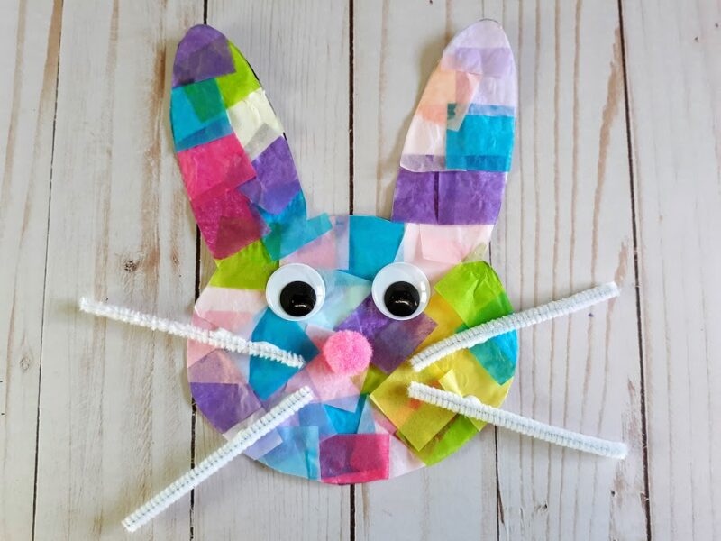 Overhead view of finished bunny suncatcher made with tissue paper, googly eyes, pink pom pom ball, and white pipe cleaner whiskers.