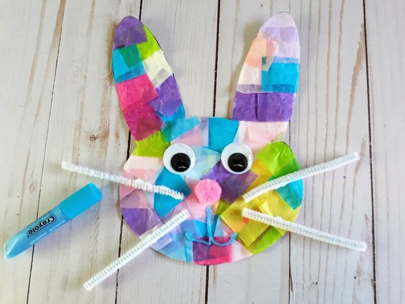 Overhead view of completed bunny suncatcher with a blue glitter glue mouth added. A blue glitter glue pen laying next to the bunny head.