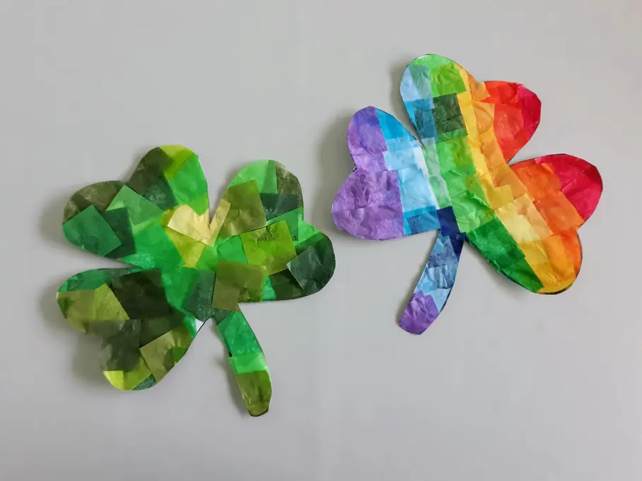 Two finished shamrock suncatchers cut out from template. Left one in various shades of green and the right one is rainbow.