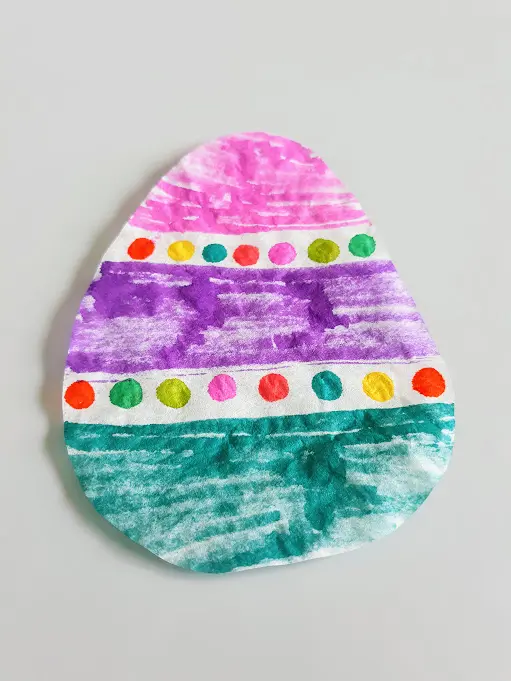Close overhead view of coffee filter cut into egg shape with pretty Easter egg design colored with markers.