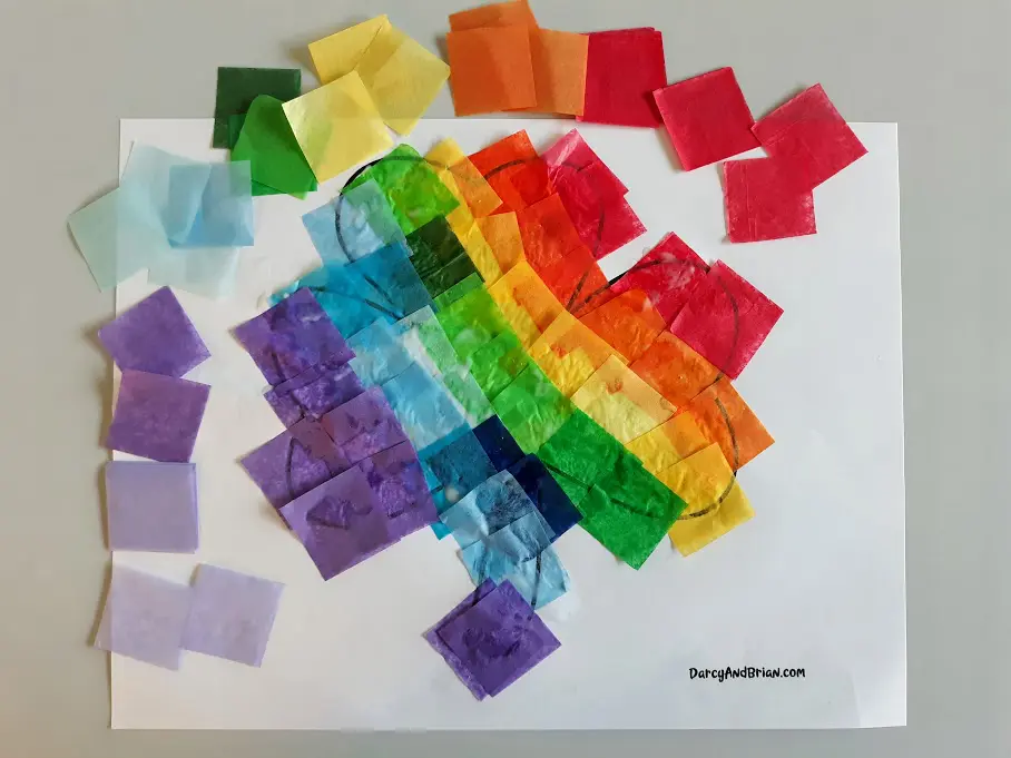 Tissue paper squares arranged in rainbow order around printable shamrock template covered in glued on tissue paper.