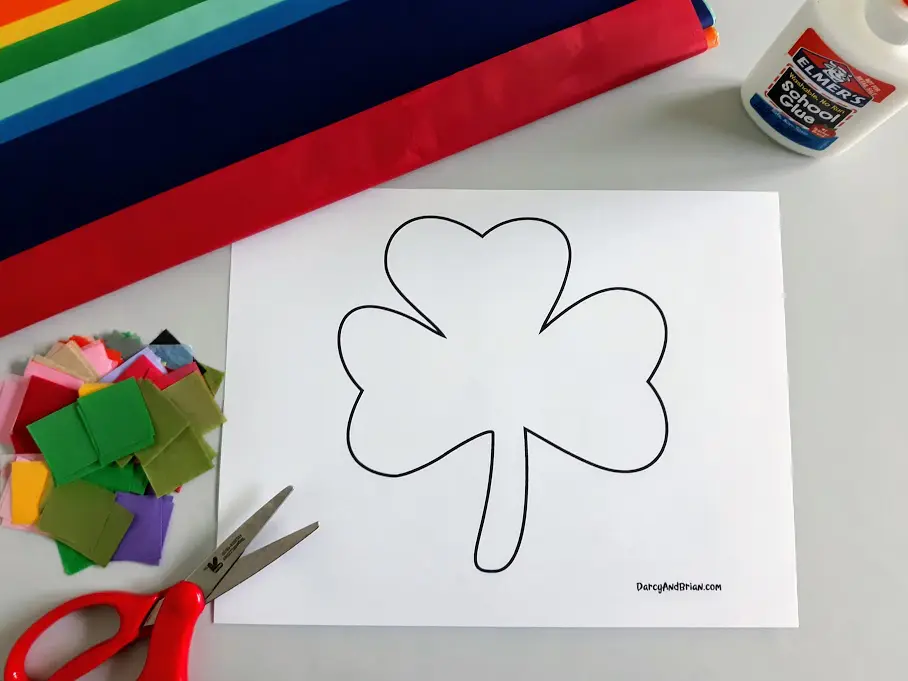 Shamrock template printout laying on craft table with scissors, tissue paper, and glue around it.
