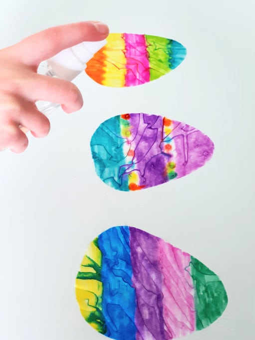 Three colored coffee filter eggs in a vertical row being sprayed with water.