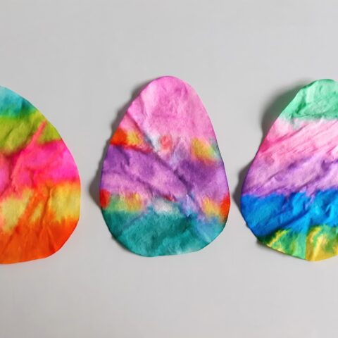 Three finished coffee filter Easter eggs laying next to each other in a row after drying.