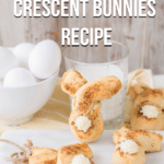 Three baked cinnamon twist bunnies laying across small white cutting board and table. One bunny shaped crescent roll propped up against glass of milk next to a small bowl of eggs. Top of picture has black and white text that reads: Easy Cinnamon Twist Crescent Bunnies Recipe.