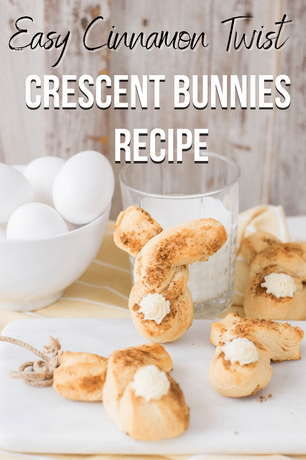 Three baked cinnamon twist bunnies laying across small white cutting board and table. One bunny shaped crescent roll propped up against glass of milk next to a small bowl of eggs. Top of picture has black and white text that reads: Easy Cinnamon Twist Crescent Bunnies Recipe.