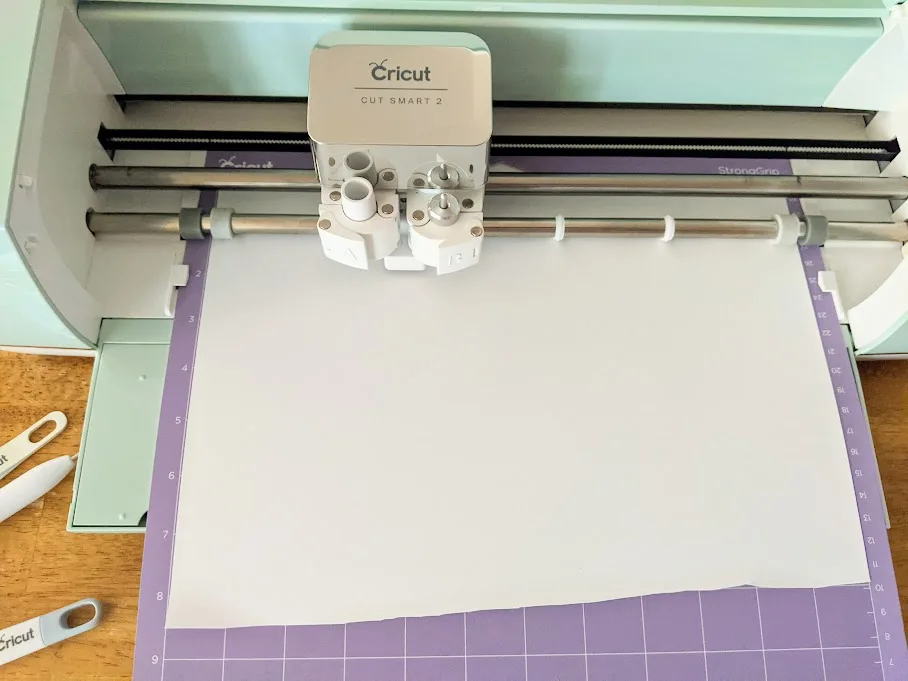 Mint Cricut Explore Air 2 cutting machine open with purple mat loaded with white iron on vinyl. Blade is cutting design.