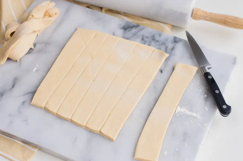 Crescent dough rolled out on white marble cutting board and cut into strips.
