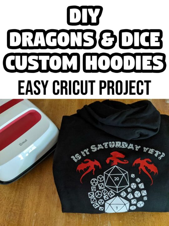 Black and white text says DIY Dragons & Dice Custom Hoodies Easy Cricut Project above photo of folded black hoodie showing design on the back with dragons, dice, and Is it Saturday yet? Hoodie is next to Cricut EasyPress 2 on a table.
