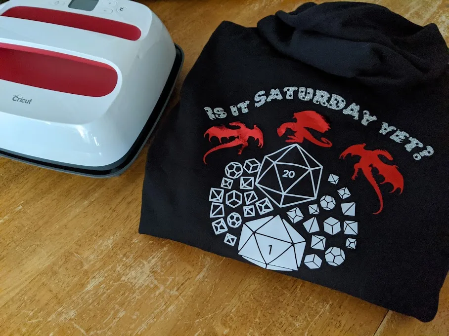 Completed custom hoodie with dragons and dice folded on table next to EasyPress 2.