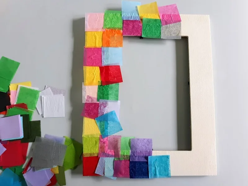 Overhead view of photo frame half covered in tissue paper squares. They are hanging over the inner edge.