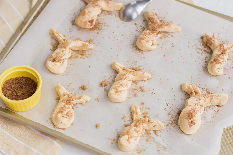 Crescent bunny twists arranged on baking sheet and sprinkled generously with cinnamon sugar mixture before baking.