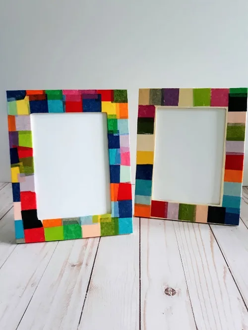 Two completed picture frames decorated with multi-colored tissue paper standing up.