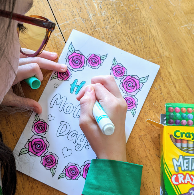 Over the shoulder view of white girl coloring the printable Mother's Day card with markers and crayons.