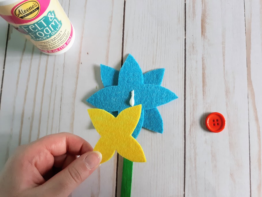 White woman's hand gluing yellow felt petals to blue felt flower.