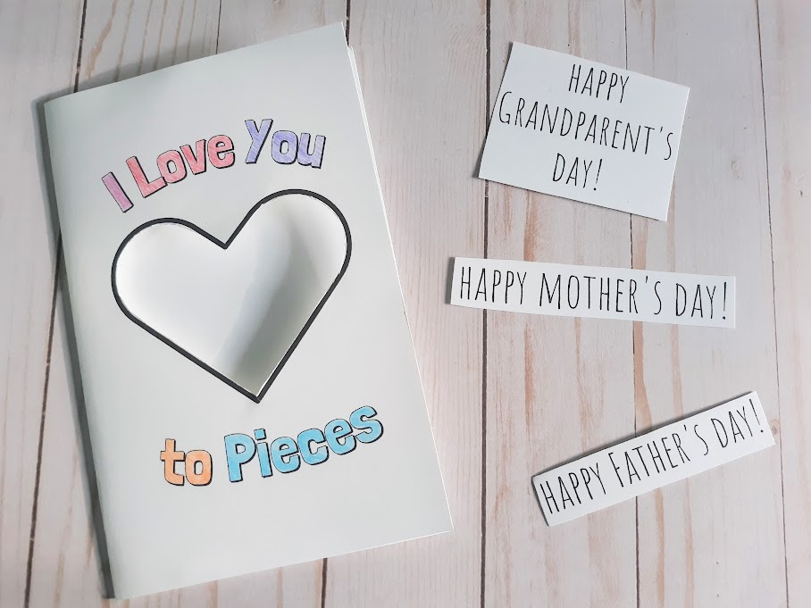 Overhead view of I Love You to Pieces printable card with words colored in and heart shape cut out. Phrases that can be glued inside card laying next to it read: Happy Grandparent's Day! Happy Mother's Day! Happy Father's Day!