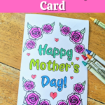 Top has white text outlined with black on a bright pink rectangle. Text reads Printable Mother's Day Card. Below text is a printed out card that says Happy Mother's Day colored in with blue and green marker. Words are surrounded by roses and small hearts colored in with crayons. Several crayons lay by card on table.