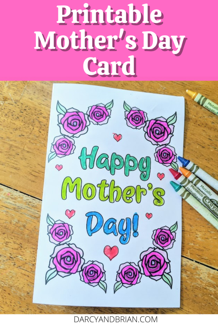 Top has white text outlined with black on a bright pink rectangle. Text reads Printable Mother's Day Card. Below text is a printed out card that says Happy Mother's Day colored in with blue and green marker. Words are surrounded by roses and small hearts colored in with crayons. Several crayons lay by card on table.