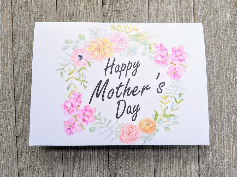 Overhead view of printable Mother's Day card printed out and folded. Front of card has a wreath of pink, yellow, and orange flowers with Happy Mother's Day in the center.