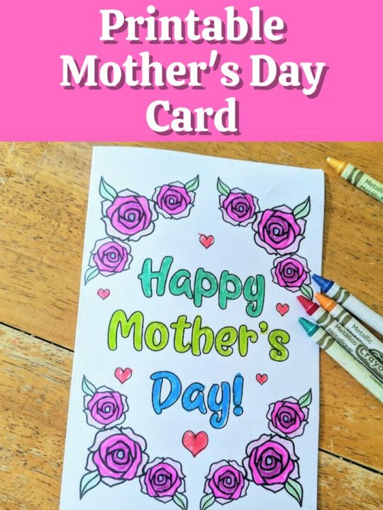 Top has white text outlined with black on a bright pink rectangle. Text reads Printable Mother's Day Card. Below text is a printed out card that says Happy Mother's Day colored in with blue and green marker. Words are surrounded by roses and small hearts colored in with crayons. Several crayons lay by card on table.