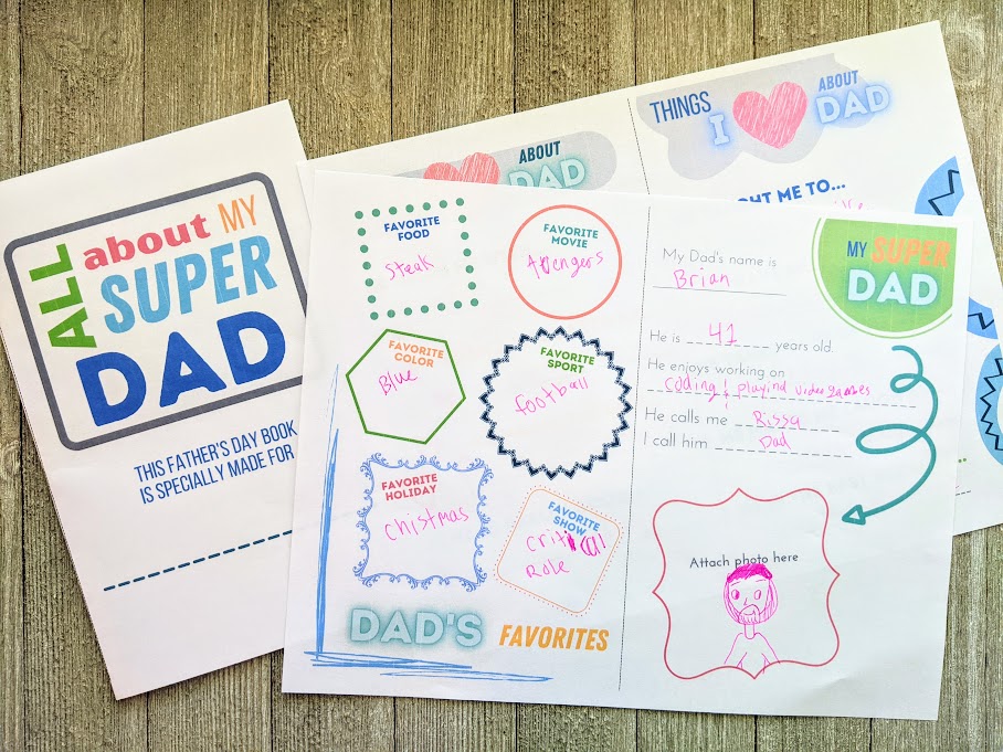 All About My Super Dad cover page printed out, folded in half, and laying next to two printed out questionnaire pages filled out with a pink gel pen.