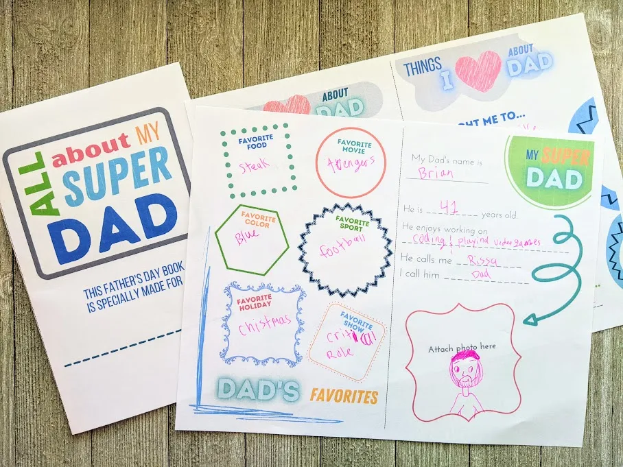 All About My Super Dad cover page printed out, folded in half, and laying next to two printed out questionnaire pages filled out with a pink gel pen.