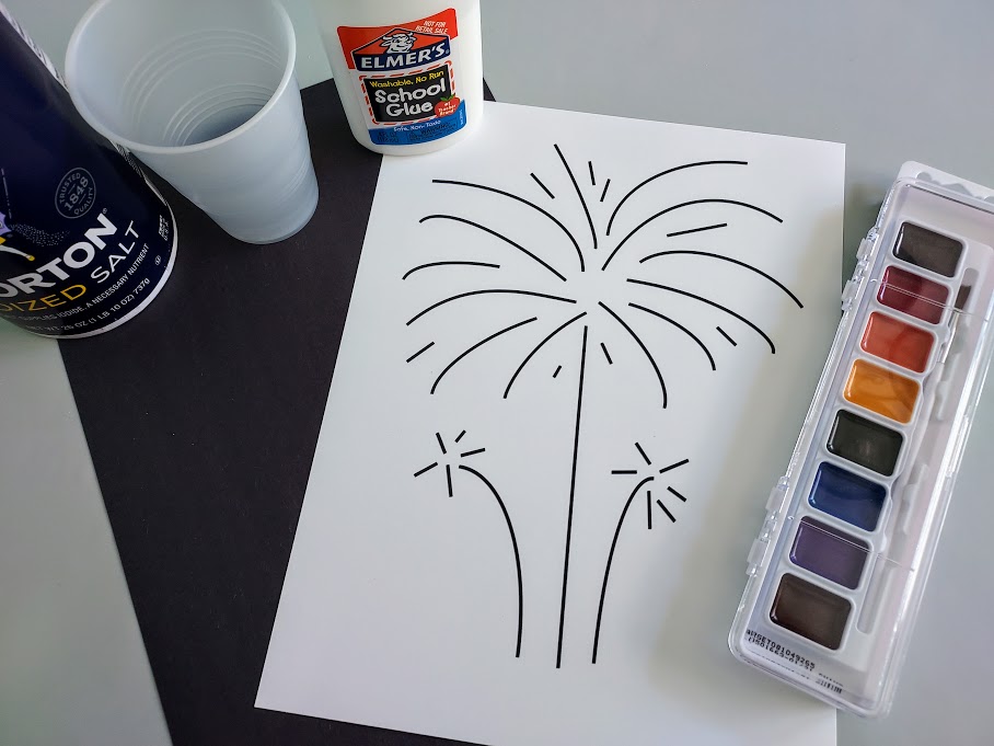 Overhead view of printed out fireworks template on white cardstock, a piece of black construction paper, water colors, liquid glue, cup of water, and container of table salt.