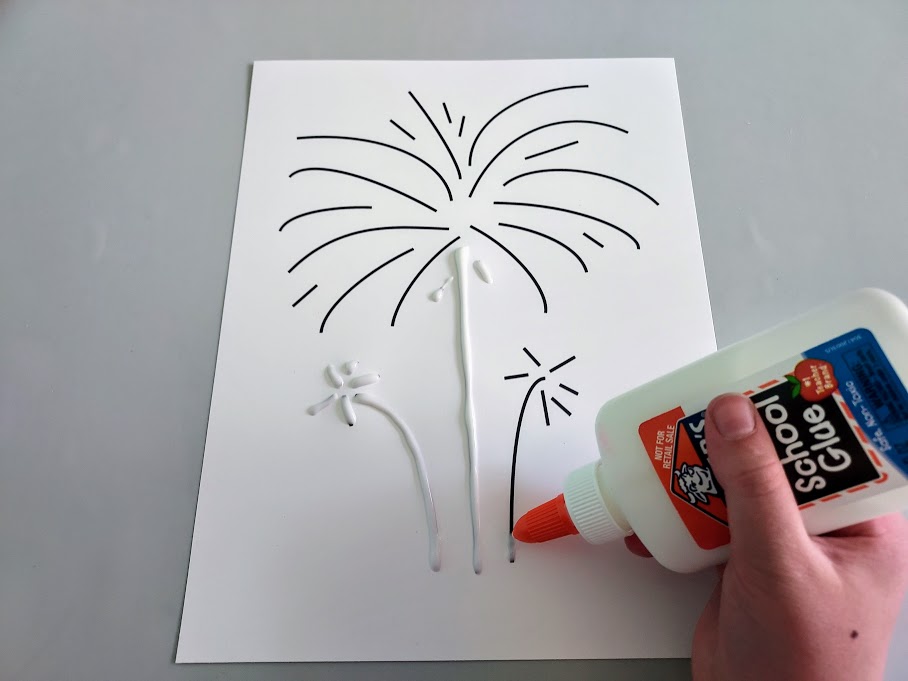 White girl's hand holding liquid glue bottle and squeezing glue along black lines of fireworks template.