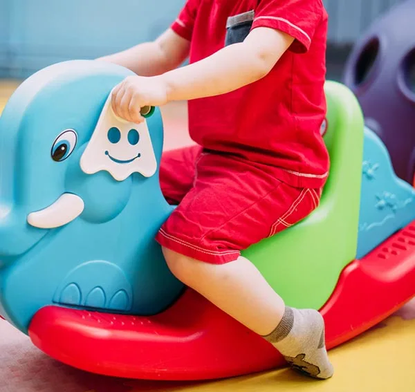 Side view of a toddler in red outfit from shoulders down on a rocking elephant toy.