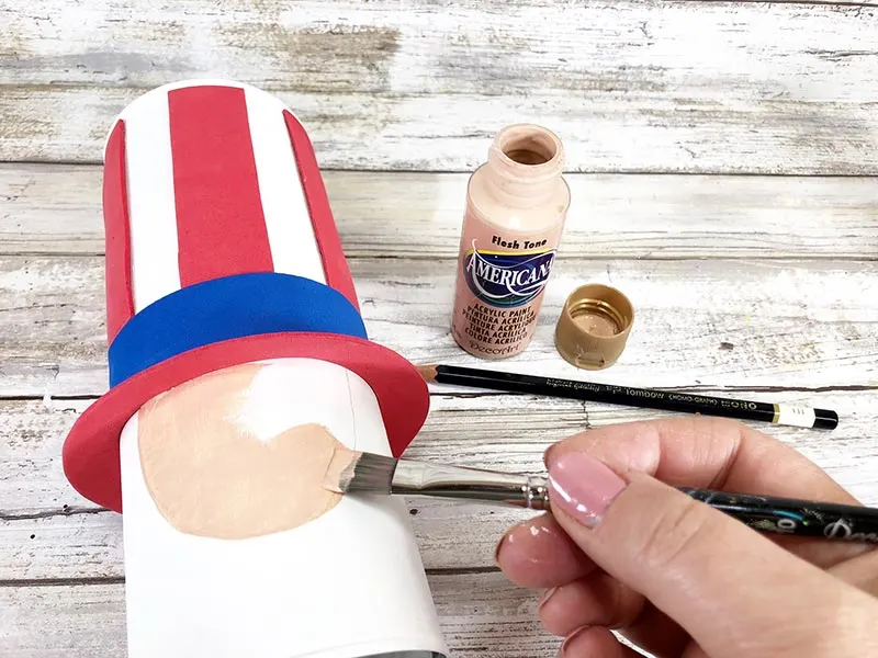 White woman's hand painting Uncle Sam's face onto chip can.