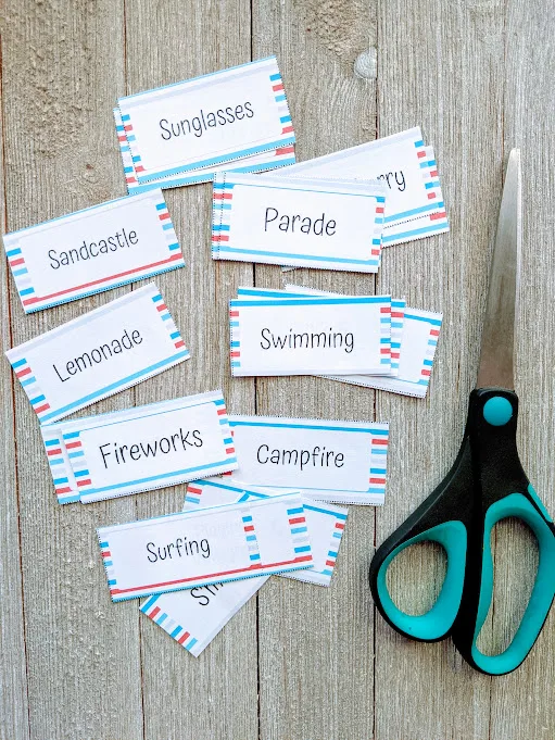 Summer themed drawing prompt cards cut apart and spread out on gray wooden table next to pair of scissors.