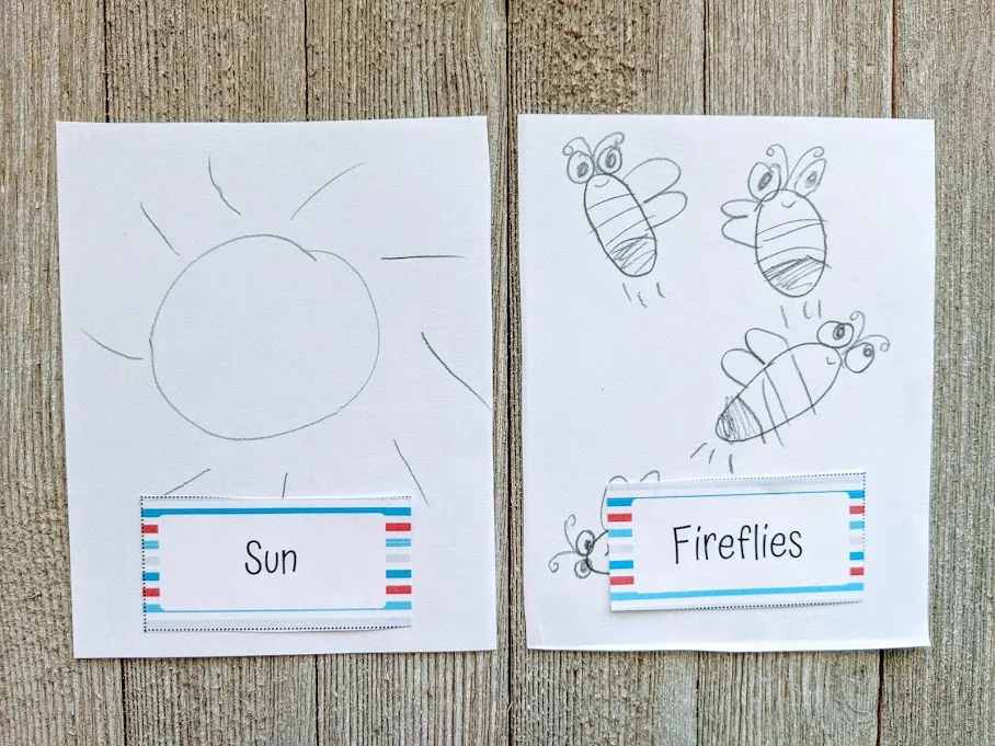 A sun and fireflies drawn in pencil by a child with the pictionary card laying at bottom of the drawings.