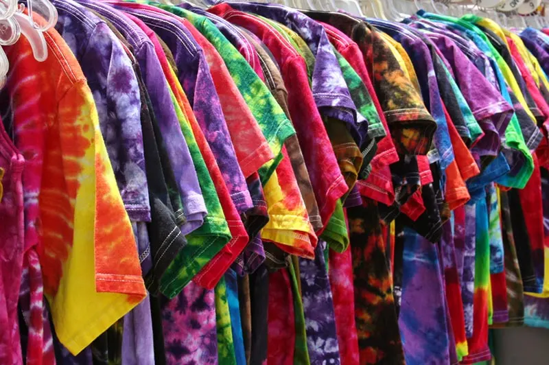 Angled side view of lots of tie dyed shirts on a clothing rack.