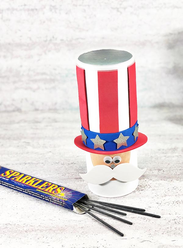 Completed Uncle Sam chip can craft project standing up next to a small box of sparklers with some of the sparklers spilling out.