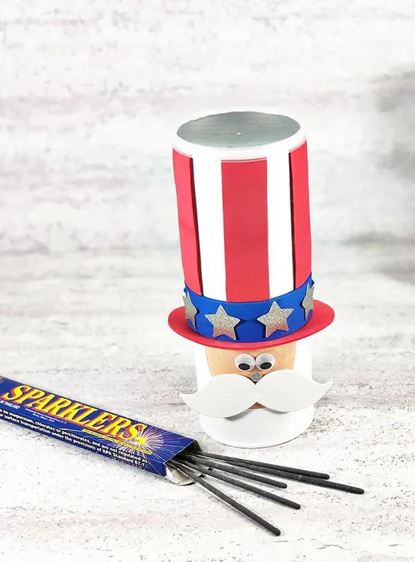 Completed Uncle Sam chip can craft project standing up next to a small box of sparklers with some of the sparklers spilling out.