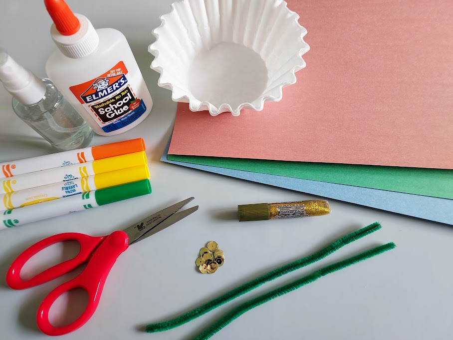 Various colors of construction paper, coffee filters, green chenille stems, sequins, glitter glue, scissors, orange, yellow, and green markers, and liquid glue on table.