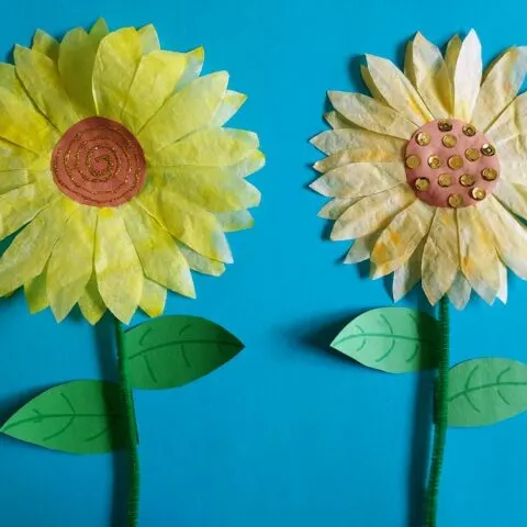 two completed coffee filter sunflower crafts on blue paper.