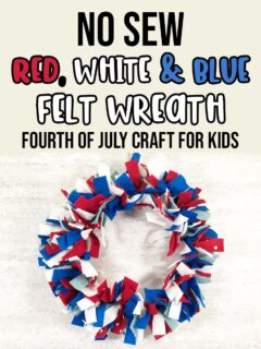 A picture of a felt wreath made with red, white, dark blue, and light blue felt strips hanging against an off white brick wall. Above wreath text in black, red, white, and blue says No Sew Red, White & Blue Felt Wreath Fourth of July Craft for Kids.