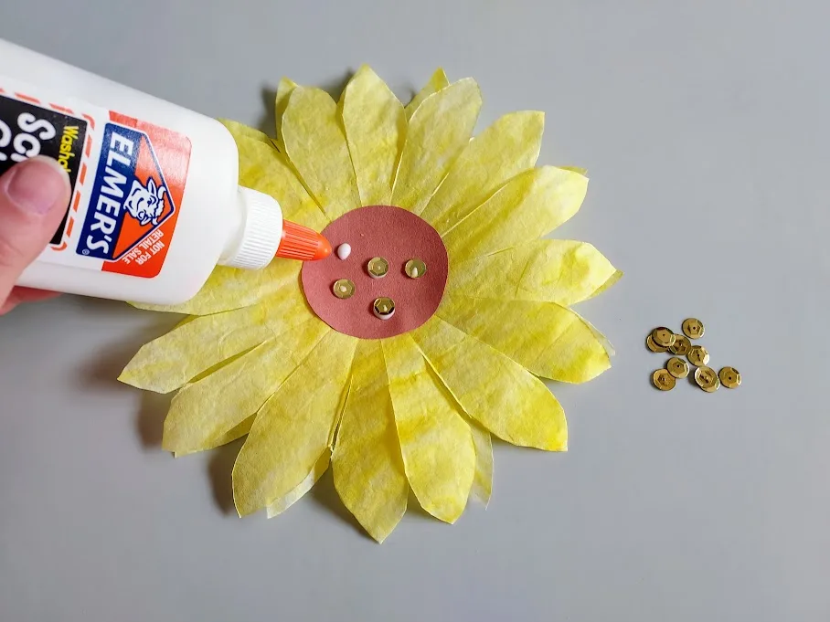 Gluing gold sequins to center of coffee filter sunflower art project.