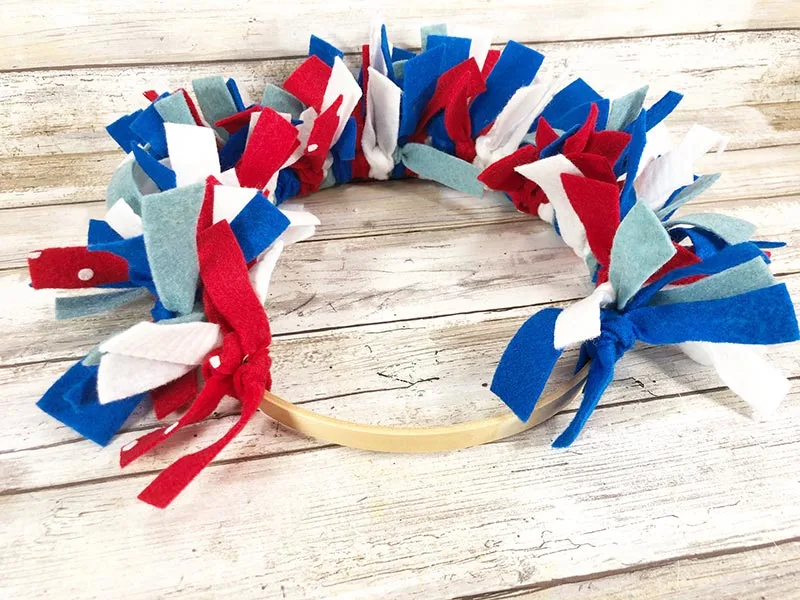 Wooden embroidery hoop almost full of tied on felt strips in red, white, and blue colors to make wreath for 4th of July.