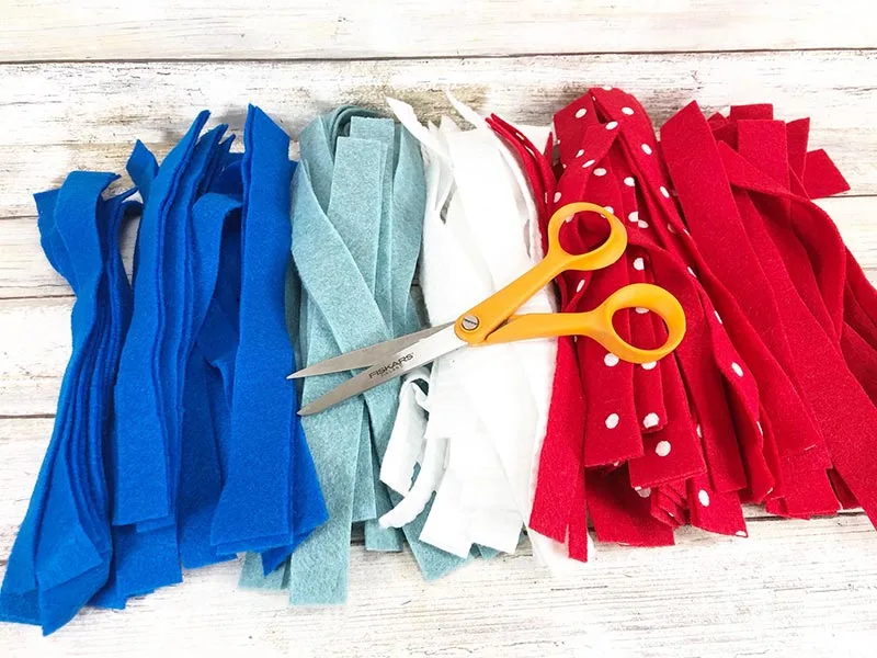 Piles of dark blue, light blue, white, red with white dots, and red felt strips with pair of scissors laying on top.