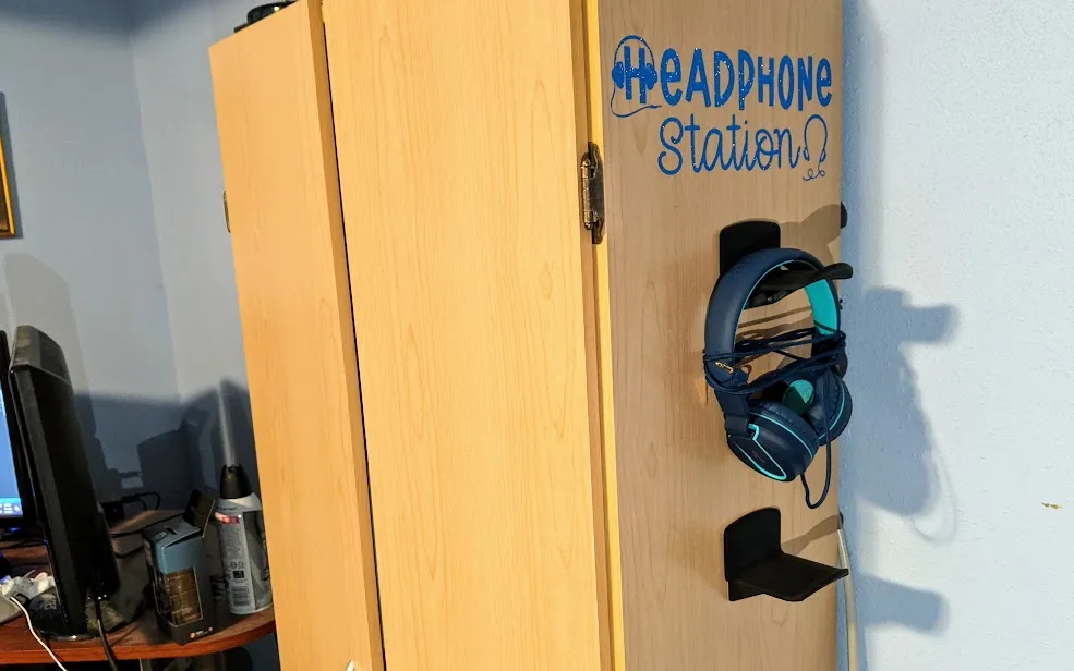 Finished DIY headphone station from angled side view to show blue vinyl Headphone Station design on the side of cabinet with headphones on hanging hooks below design in computer gaming room.