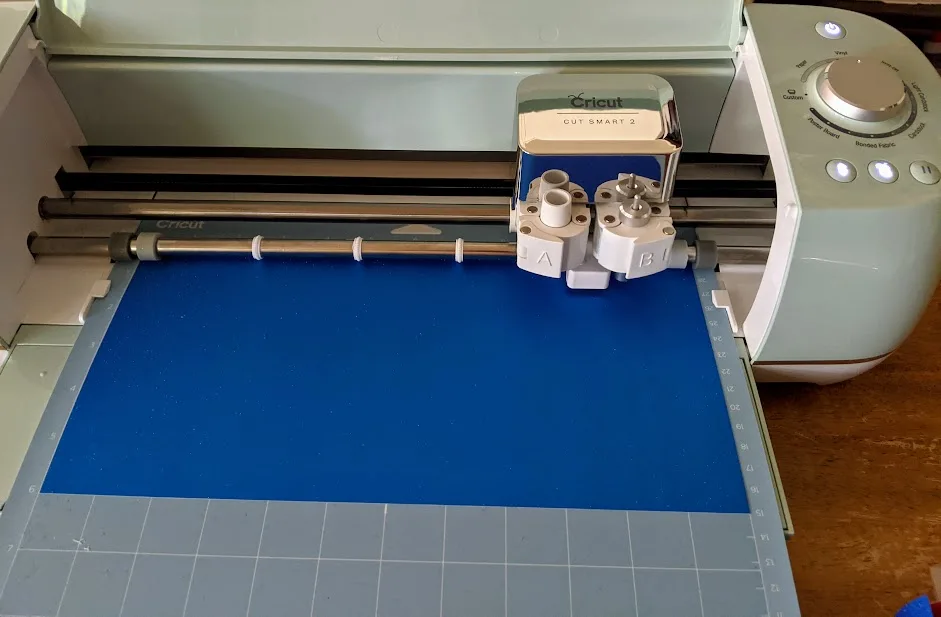 Machine mat with blue shimmer vinyl on it loaded and being cut by Cricut Explore Air 2 cutting machine.