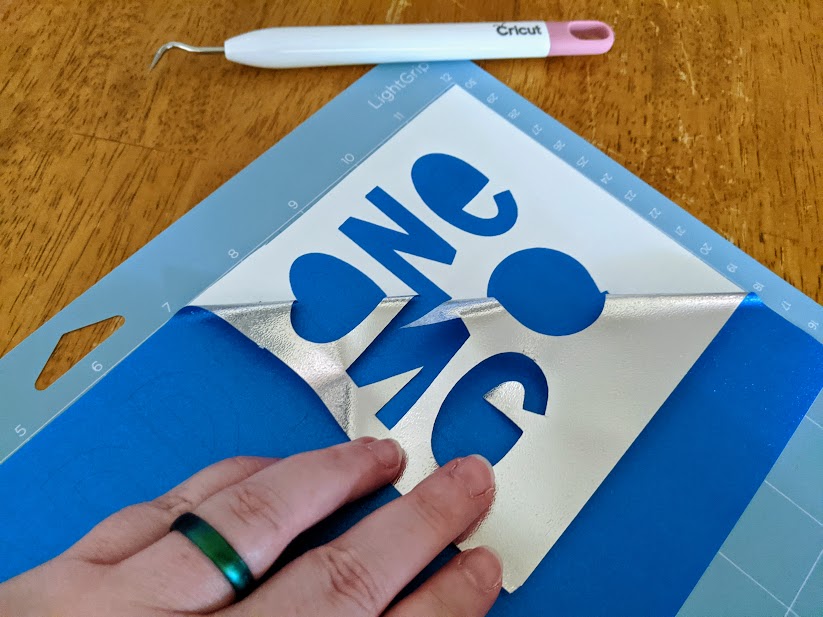 White woman's left hand with green silicone ring on ring finger peeling back excess vinyl from design.