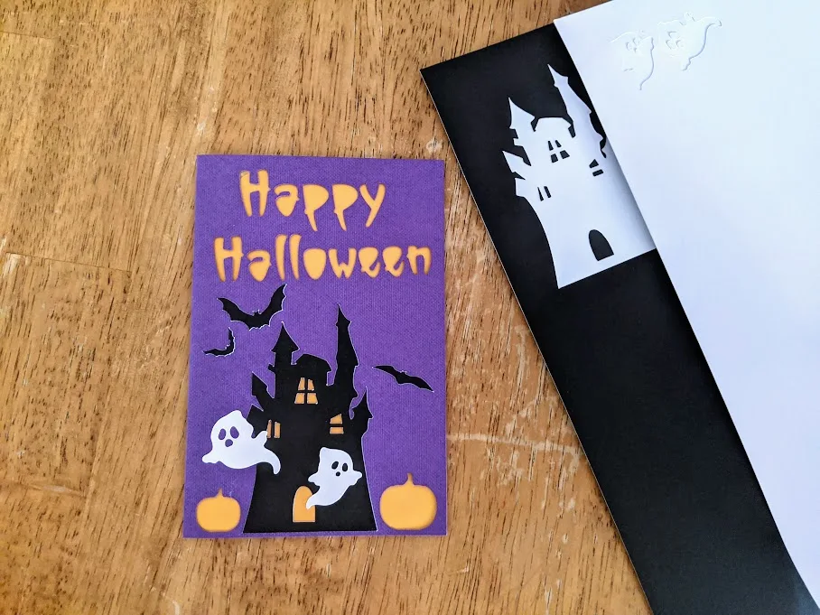 Overhead view of Halloween card project with white sticker cardstock ghosts added to the front. Card is laying next to the sticker cardstock and can see where designs were removed.