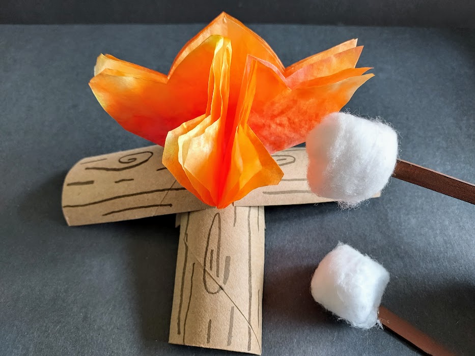 Pretend play with campfire made out of orange colored coffee filters and cardboard tube logs with cotton ball marshmallows on brown craft sticks.