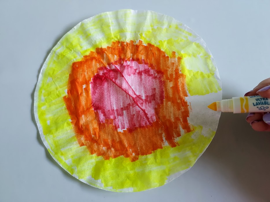 Round coffee filter colored with markers: red in the center, then a ring of orange, and yellow on the outer edge.
