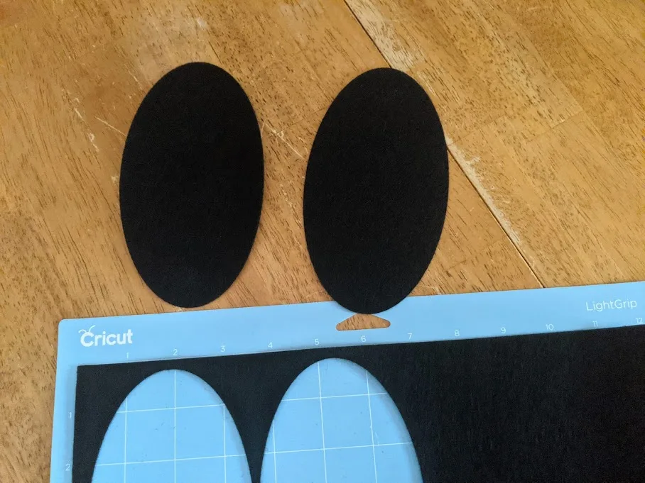 Two felt ovals cut out using cutting machine laying on table next to machine mat with the rest of the felt material.