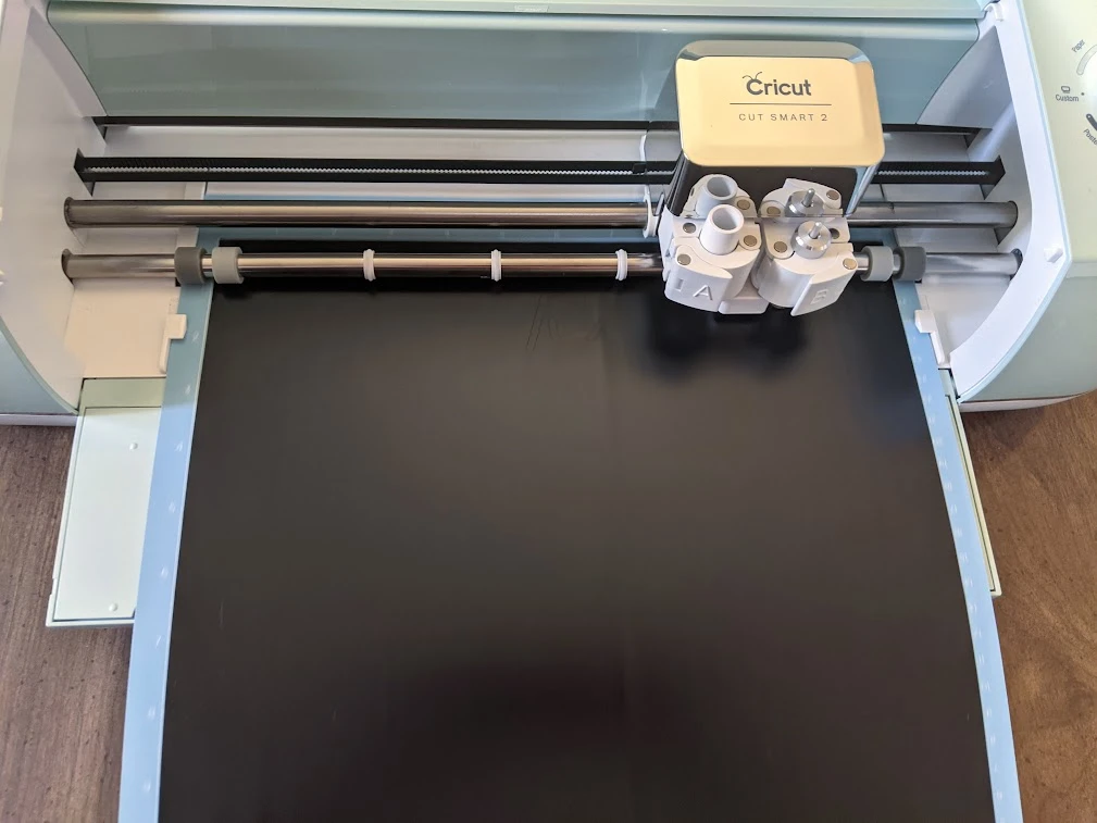 Machine mat with black vinyl loaded into Cricut cutting machine.
