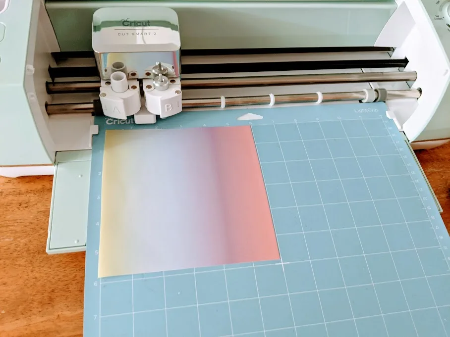 Rainbow infusible ink transfer sheet on a blue cutting mat loaded into Cricut cutting machine.